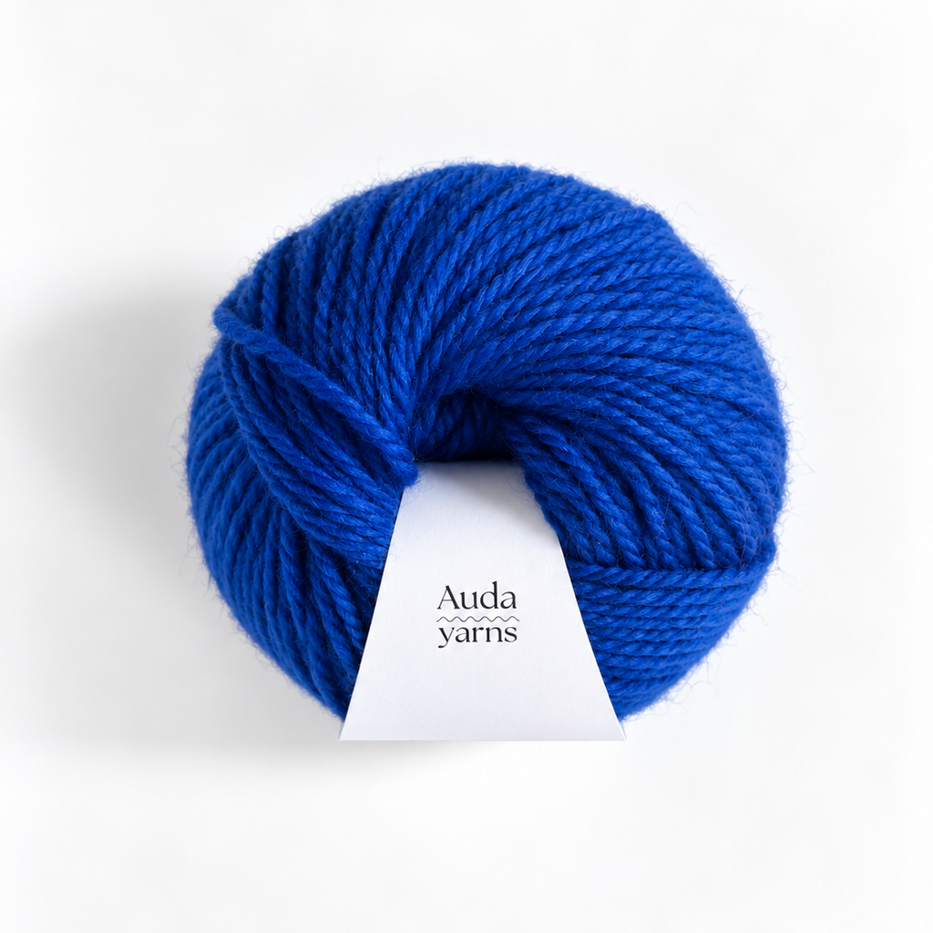 A skein of vibrant royal blue yarn with a white paper label reading 'Auda yarns', photographed on a clean white background.