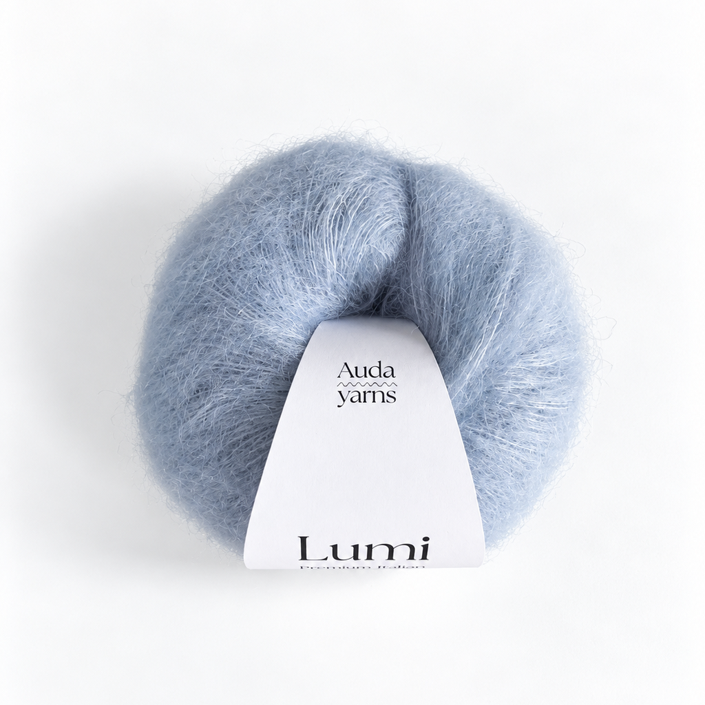 A skein of fluffy light blue yarn with a white paper label that reads 'Auda yarns Lumi' on a clean white background.