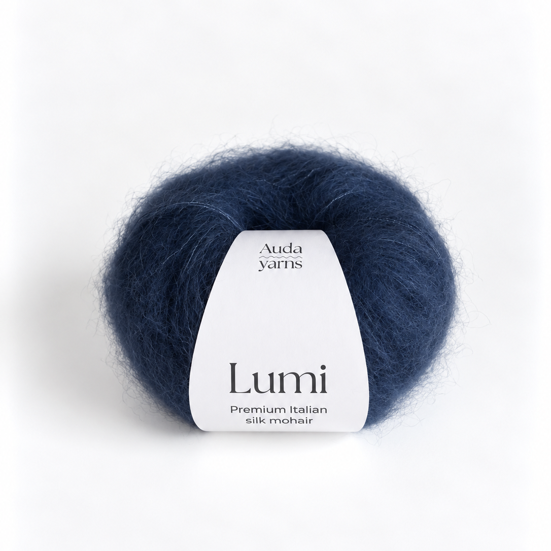 A ball of Lumi silk mohair yarn in a deep navy blue color, featuring a white paper label with the brand name 'Auda Yarns' on a clean white background.