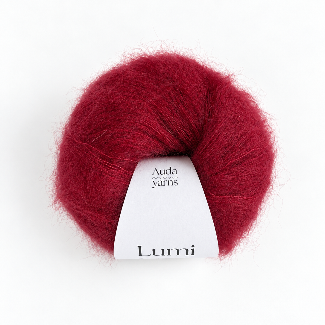 A ball of deep burgundy red yarn with a white paper label that reads 'Auda yarns Lumi', centered on a clean white background.